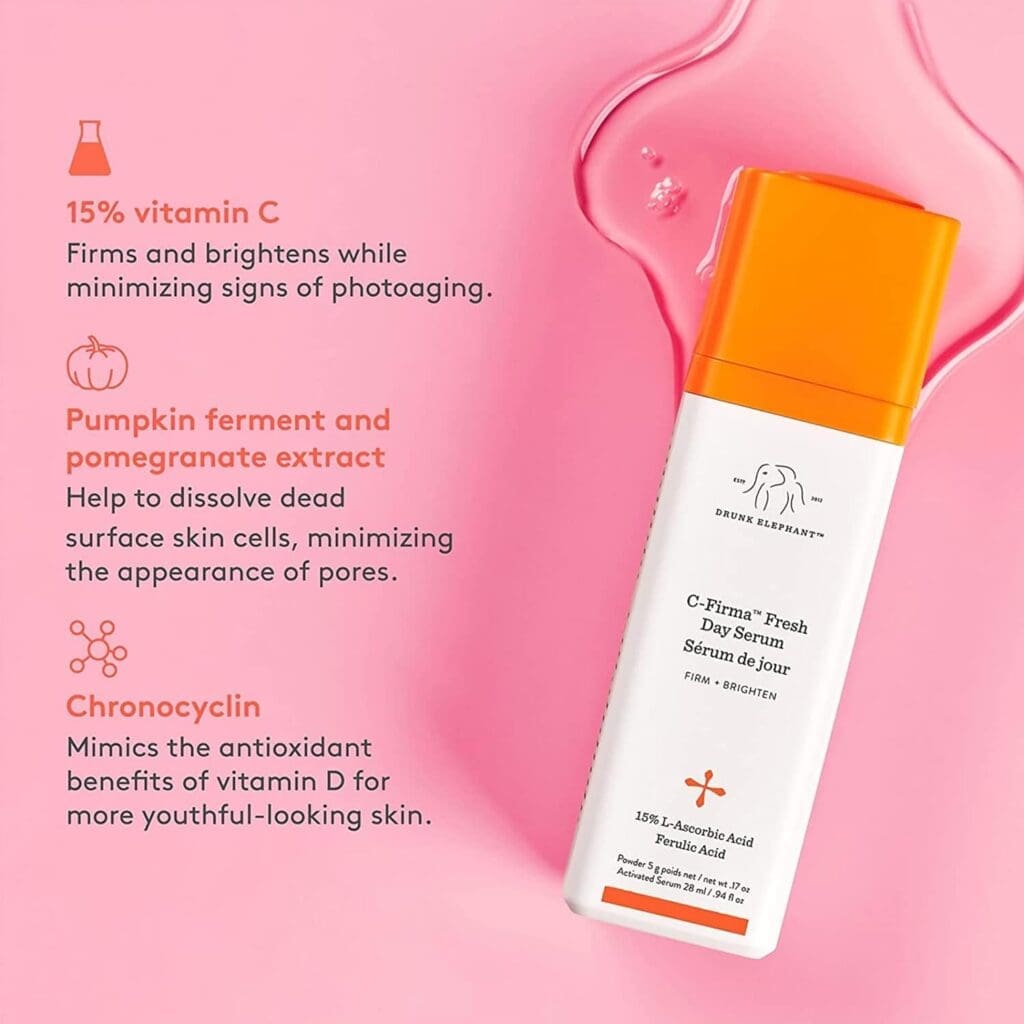 A bottle of Drunk Elephant C-Firma Fresh Day Serum with an orange cap is placed on a pink background with serum droplets. The text highlights key ingredients, including 15% Vitamin C for firming and brightening, pumpkin ferment and pomegranate extract for exfoliation and pore minimization, and Chronocyclin, which mimics Vitamin D's antioxidant benefits for youthful-looking skin.