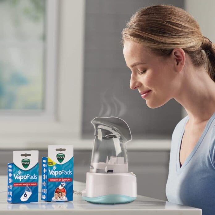 A woman using the Vicks V1200 Personal Steam Inhaler, enjoying soothing steam therapy for sinus relief, with Vicks VapoPads displayed nearby to enhance the inhalation experience.