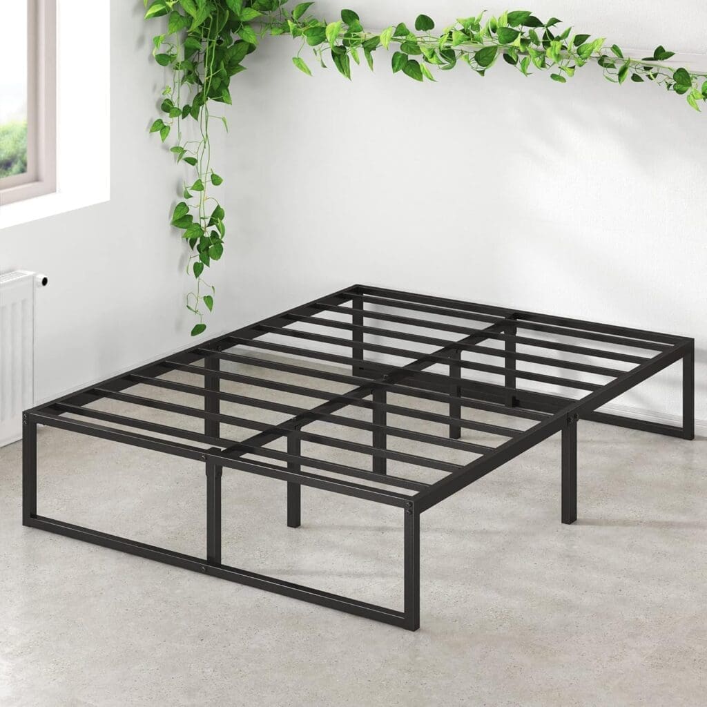 A minimalistic black steel platform bed frame with a sturdy, low-profile design. The bed frame is set against a white wall with green vine decorations, showing its strong metal slats and under-bed storage potential.